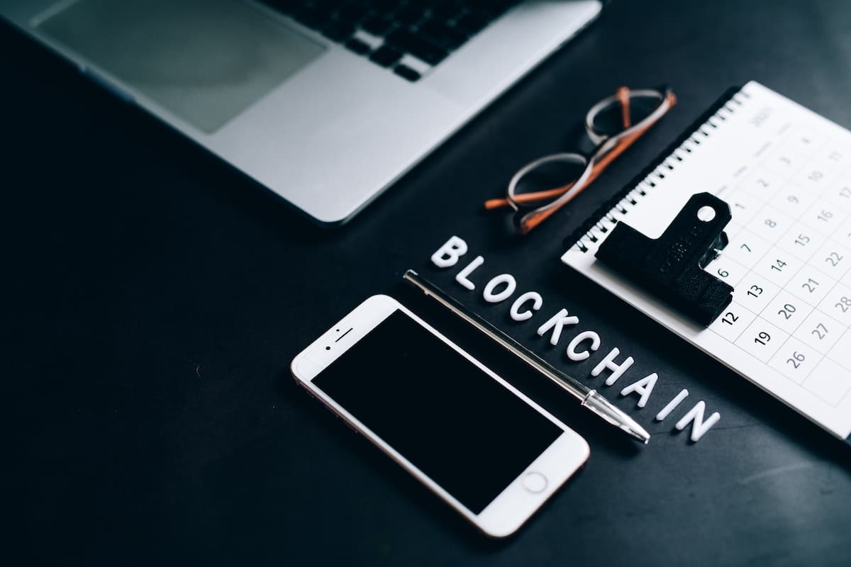 Desk with cellphone, calendar, glasses, pen and letters spelling out blockchain.