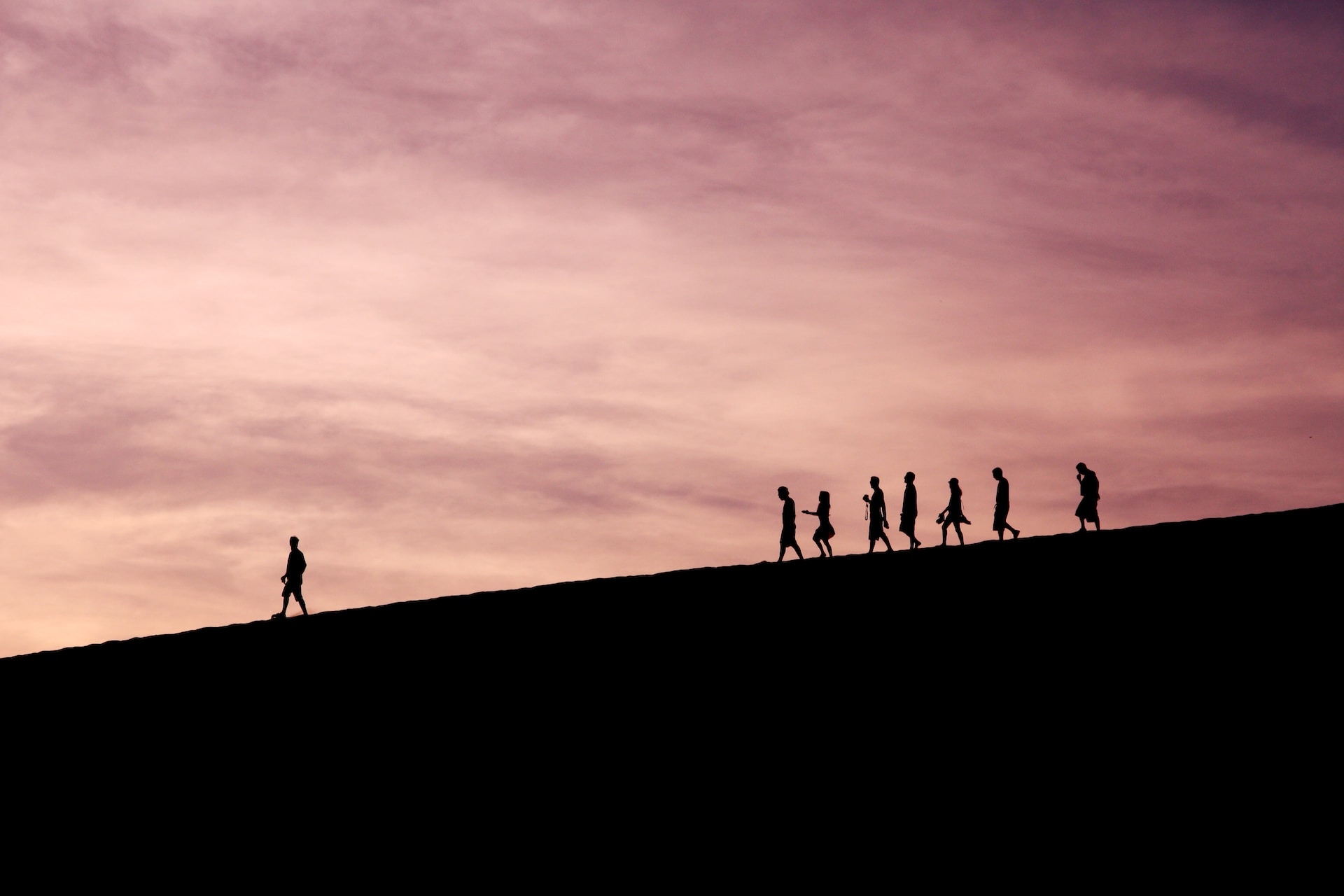 Silhouette of one person walking ahead of seven other people.