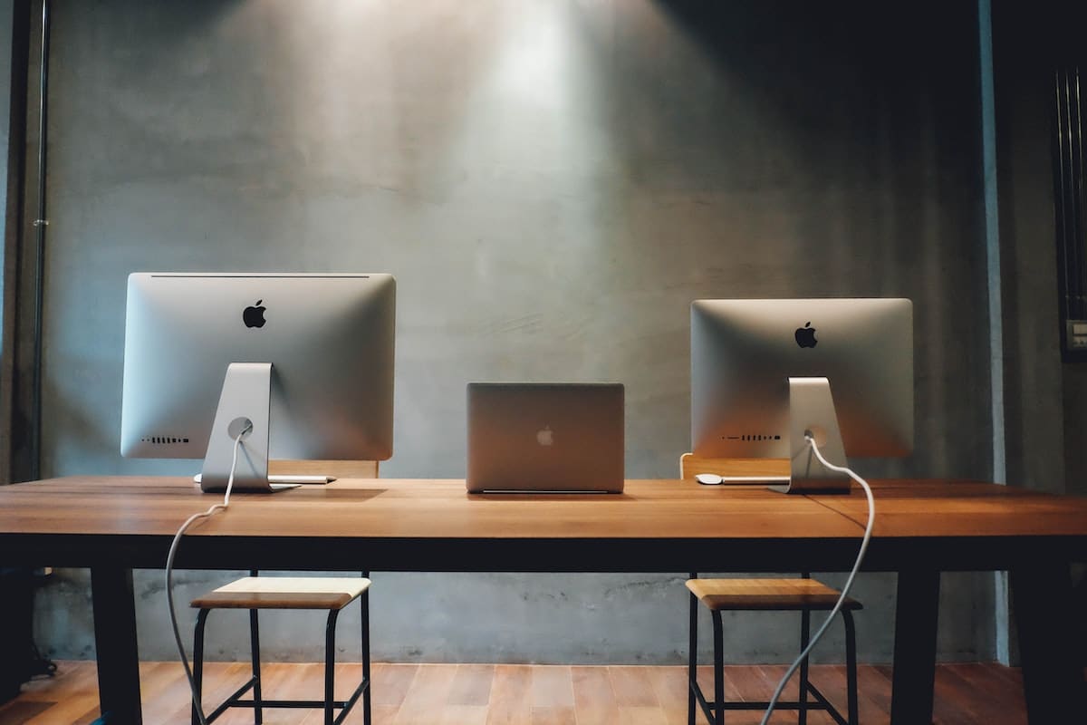 Two Imac and a Macbook on a table.