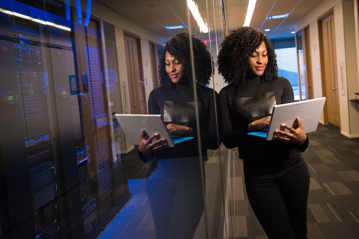 Woman holding a laptop leaning against a glass window.