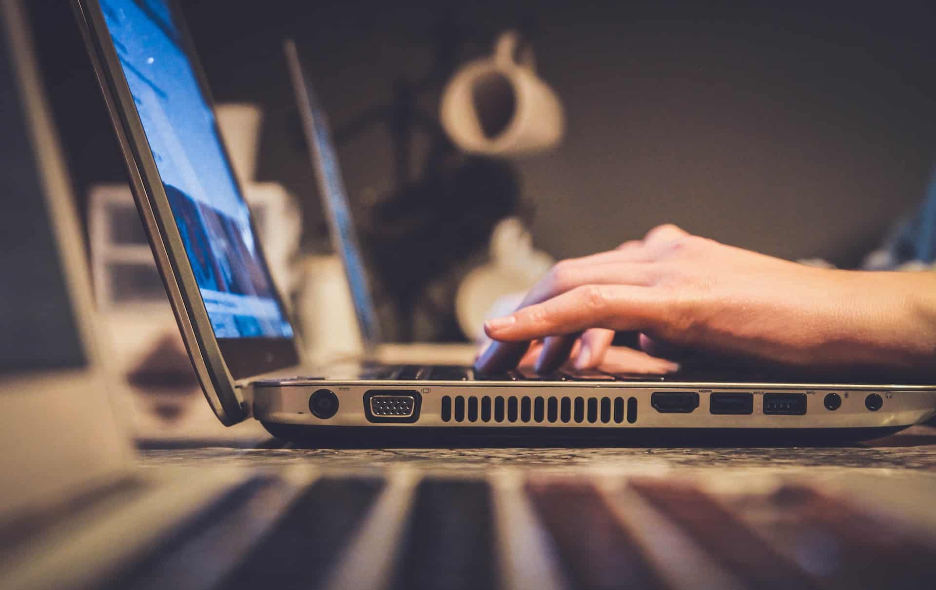 Image of a laptop on a desk with hands typing on it.