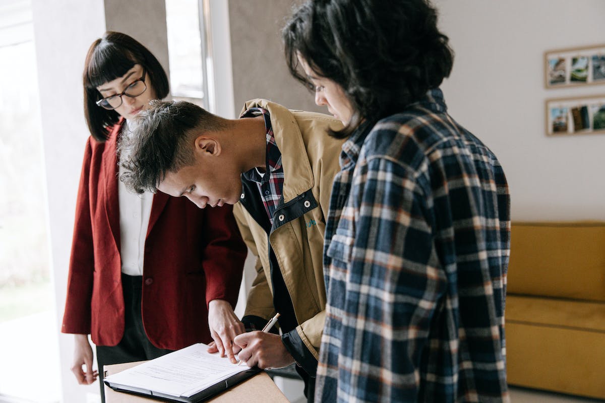 Man Signing Documents Beside Woman and Real Estate Agent